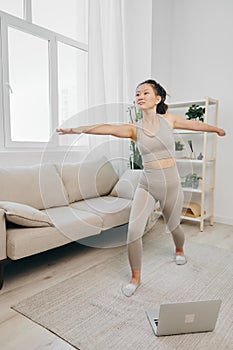 Asian woman at home exercising stretching and yoga repeating complex asanas and exercises online while looking at her