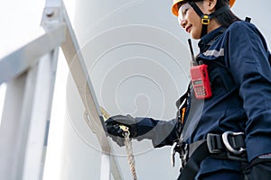 Asian woman Inspection engineer wearing safety harness and safety line working preparing and progress check of a wind turbine with