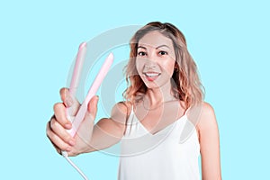 Asian woman with iron ceramic hair curler posing in studio