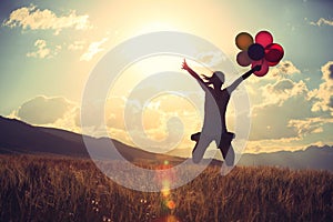 Asian woman jumping on sunset grassland with colored balloons