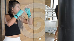 Asian woman kick boxer punching and kicking bag in gym