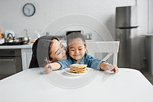 Asian woman kissing smiling daughter near