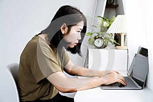 Asian woman with Kyphosis: side view of laptop Work with hunched back, forward head posture, and spinal curvature