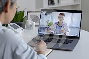 Asian woman with laptop during an online consultation with her doctor in her living room, telemedicine concept.