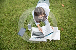 Asian woman lay down green garden park using laptop working outdoor home office. Happiness Woman smile working Freelance on laptop