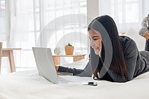 Asian woman laying on bed doing paperwork on laptop in bedroom.work at home.e-larning concept.study online. photo