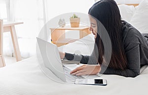 Asian woman laying on bed doing paperwork on laptop in bedroom.work at home.e-larning concept.study online photo