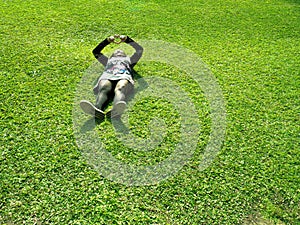 Asian woman is laying on the green grassland. Young lady is wearing flowers and black dress. Pretty female romantic making a heart