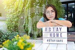 Asian woman with a lightbox sign with text hashtag  STAY HOME and  STAY SAFE. COVID-19. Stay home save concept