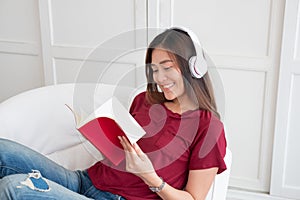 Asian woman listening music on headphone and reading book with relax pose at couch in living room at home.leisure lifestyle