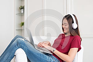 Asian woman listening music on headphone and using laptop computer with relax pose at couch in living room at home.leisure