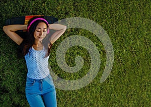 Asian Woman Listening To Music With Headphones And Laying On A Grass Field
