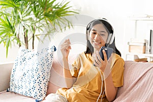 Asian woman listening to music on smartphone with headset enjoy. Asia woman using mobile phone happy smile while sitting on sofa