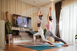 Asian woman and Little girl practicing yoga from yoga online course via smart TV at home. Healthy lifestyle - technology at home.