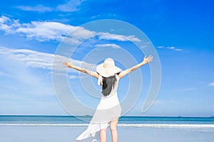 Asian woman, long black hair, wore white dress and hat standing at the beach,arms open and facing back by the sea with copy space