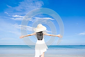 Asian woman, long black hair, wore white dress and hat standing at the beach,arms open and facing back by the sea with copy space