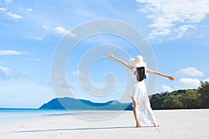 Asian woman, long black hair, wore white dress and hat standing on the beach near the woven bags and sunglasses and facing back by