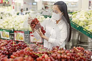 Asian woman long hair wearing protective face mask  in supermarket department store. Female, looking grocery to buy  some fruit.