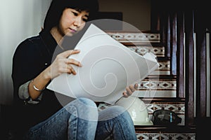 Asian woman looking architectural plan, sitting on the stairs and working at home