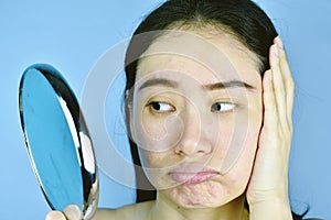 Asian woman looking at her facial problem in the mirror, Female feeling annoy about her reflection appearance show the aging skin.