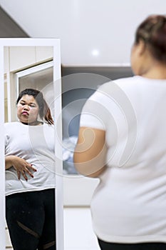 Asian woman looking at her fat belly in a mirror