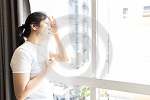 Asian woman looking out window at strong sunlight,hot weather,high temperature heat wave,harsh ultraviolet rays of sun,risk of