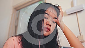an Asian woman looks lost in thought while holding a smartphone in her hand in a room