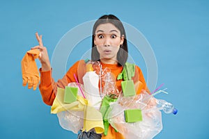 Asian woman looks shocked, holds plastic rubbish, sorting garbage for recycling, looks surprised, blue background