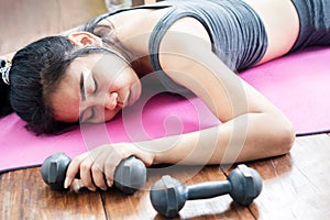 Asian woman lying down on floor feeling tired after doing sport, overtraining hand holding dumbbell