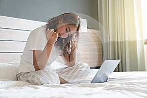 Asian woman lying down and smiling the bed and laptop