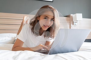 Asian woman lying down and smiling the bed and laptop