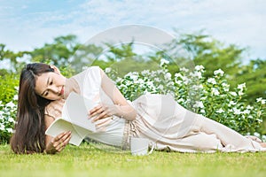 Asian woman lying on grass field for read a white book in the park , relaxation concept by beautiful asian woman
