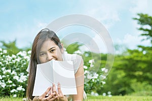 Asian woman lying on grass field with white book in the park