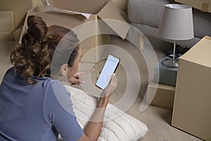 Asian woman lying in new house using smartphone buying decorations online after moving in