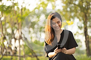 Asian woman mature using cell phone in public park. Adult female holding cell phone with beautiful sun light