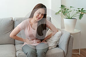 Asian woman with menstruation and pain period cramps. young women having painful sitting on sofa at her home photo