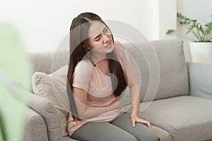 Asian woman with menstruation and pain period cramps. young women having painful sitting on sofa at her home photo