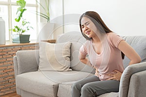 Asian woman with menstruation and pain period cramps. young women having painful sitting on sofa at her home