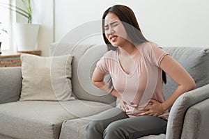 Asian woman with menstruation and pain period cramps. young women having painful while sitting on sofa at her home