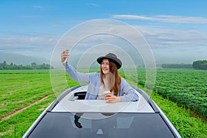 Asian woman with mobile phone and standing out of car sunroof. Relaxing and freedom with spring time. Young tourist travel