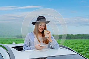 Asian woman with mobile phone and standing out of car sunroof. Relaxing and freedom with spring time. Young tourist travel