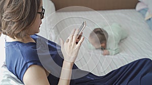 Asian woman mother busy on mobile phone ignorance baby infant crawling on bed. mobile phone addict ignore surrounded people