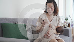 Asian woman mother holding sleeping baby infant. parent working on mobile smart phone while holding baby. new normal, covid-19 wor