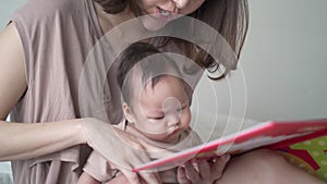 Asian woman mother parent reading storybook with baby infant. 3 months old kid learning development skill from mom with relationsh