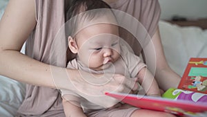 Asian woman mother parent reading storybook with baby infant. 3 months old kid learning development skill from mom with relationsh