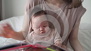 Asian woman mother reading storybook with baby infant. 3 months old kid learning development skill from mom with relationship. fam
