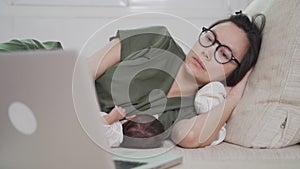 Asian woman mother working from home on computer laptop and feeding breast milk to baby infant. parent multitasking on sofa couch