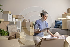 Asian woman moving into new apartment holding and unpacking her belongings with cardboard boxes