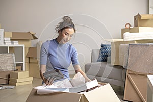 Asian woman moving into new apartment holding and unpacking her belongings with cardboard boxes
