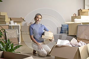 Asian woman moving into new house holding cardboard boxes with belongings, smiling and looking at camera